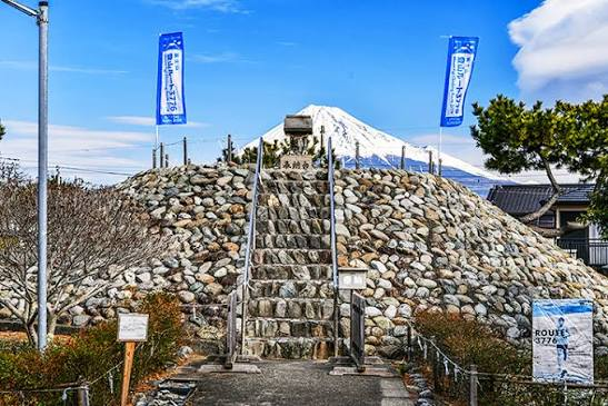 石段が組まれた富士塚の頂に、本物の富士山が重なって見える様子